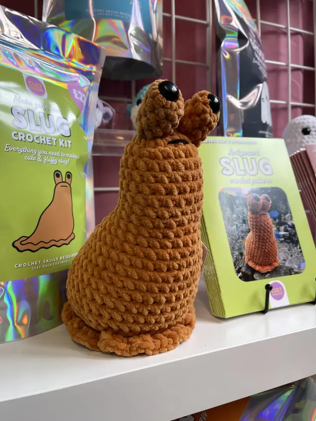 A chunky chenille crochet slug next to its Slug crochet kit